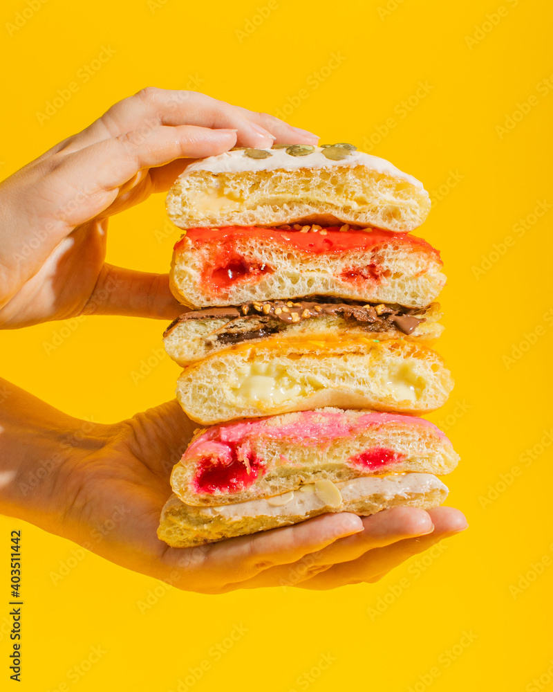 Aufkleber stack of different donuts with toppings in hands on yellow background