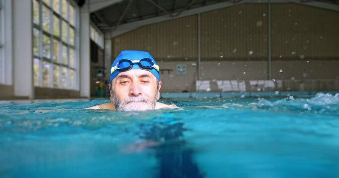 Senior man with googles and cap swimming in indoor pool