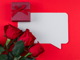 red rose and card.
Card, three roses and a gift box on a red background with a place for text in the middle, top view close-up.