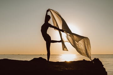 Young beautiful ballerina dancing ballet on sky and sea background with huge silk fabric. Concept...