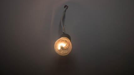 An incandescent lamp hangs on an old wire, a glowing lamp is covered in dust