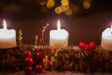 Three burning candles on a dark background with red berries, moss, succulent and pine cone