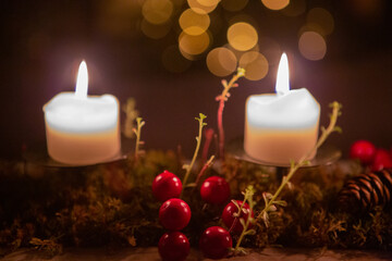 Two burning candles on a dark background with red berries, moss, succulent and pine cone