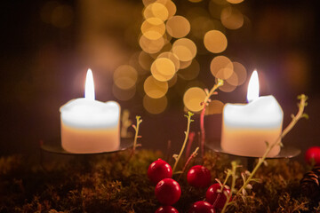 Two burning candles on a dark background with red berries, moss, succulent and pine cone
