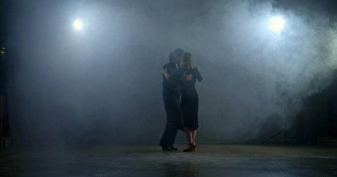 Couple dancing in the hall with smoke, elegant partner circling a beautiful woman in a black dress. Passionate dance in a dark room with fog. 4k, ProRes