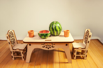 Wooden miniature dollhouse furniture, table and chairs on wooden doll floor. Crafts made of natural wood. Toy dishes,  watermelon cut in the form of and made of polymer clay.