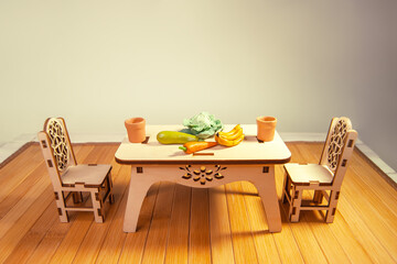 Wooden miniature dollhouse furniture, table and chairs on wooden doll floor. Crafts made of natural wood. Toy dishes,  cabbage, zucchini, carrots, bananas made of polymer clay.