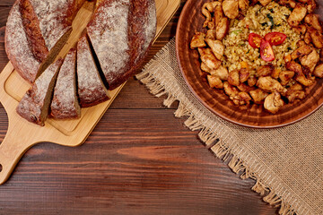 Close-up of Bulgur with chicken fillet cherry tomatoes on a plate on a wooden table. Bread sliced on a cutting board. Fork and knife top view with copy space