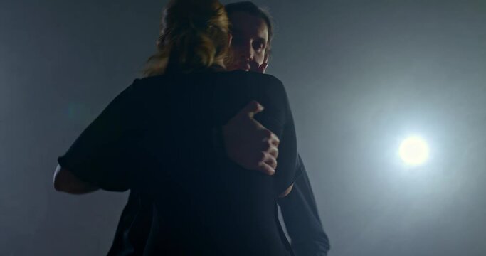 Silhouette, man and woman in pair dancing tango in a dark room with smoke, beautiful dance poses, passionate dance. Elegant man in a black suit is circling a beautiful woman in a dance, an enamored