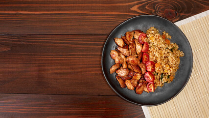 Bulgur with chicken fillet and cherry tomatoes on a plate on a wooden table. Top view with copy space