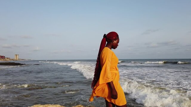 Ghana woman walking on stone cliffs on the coast of Accra in Ghana when the waves hit the cliffs
