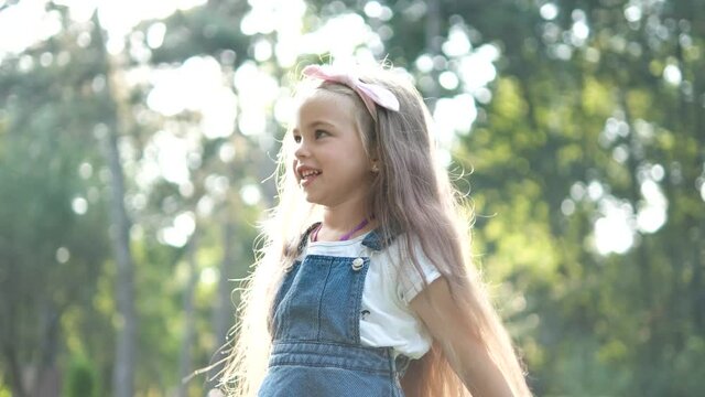 Little pretty child girl with long hair walking outdoors in green summer park on a sunny day.