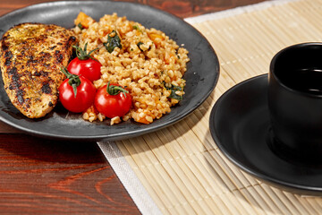 Fried chicken fillet and bulgur on a plate on a wooden background cherry tomatoes a cup with a hot drink