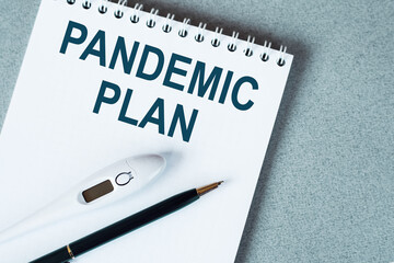 Blank notebook with thermometre and pen on table. PANDEMIC PLAN text.