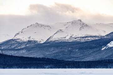 Stunning snow capped mountains in northern Canada during winter, Christmas time with a frozen lake in foreground, wilderness, woods below snowy surface. 