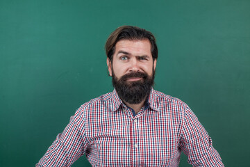 Fototapeta premium express human emotions. caucasian hipster with beard on green background. confused mature teacher on background of blackboard. brutal bearded man wear casual checkered shirt. he is so handsome