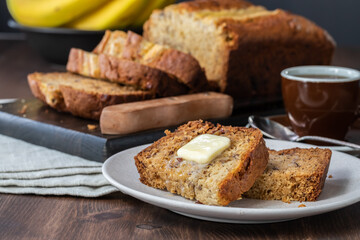 Fototapeta na wymiar Close up of slices of banana bread with butter on a small plate with a sliced banana bread loaf in behind.