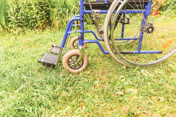 Empty wheelchair standing on grass in hospital park waiting for patient services. Invalid chair for disabled people parked outdoor in nature. Handicap accessible symbol. Health care medical concept.