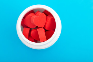 Red heart shaped pills with plastic bottle on blue background.Concept love addiction, love drugs,...