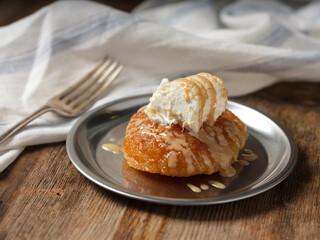 bread pudding with cream with a fork on a metal plate on wooden background