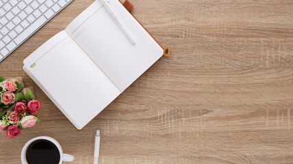 Fototapeta premium Top view wooden workspace office desk with computer and office supplies. Flat lay work table with blank notebook, keyboard, flower and coffee cup. Copy space for your advertising content.