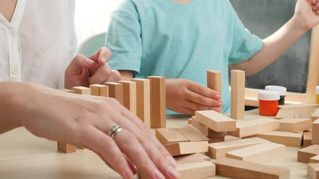 Closeup of child with mother playing with wooden blocks and bricks. Domino or chain effect. Mother educating and teaching her child at home during lockdown and self isolation. Family having fun