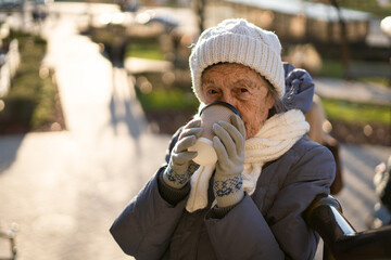 Joyful senior lady holding coffee to go, dressed winter clothes in city. Beautiful elderly lady...