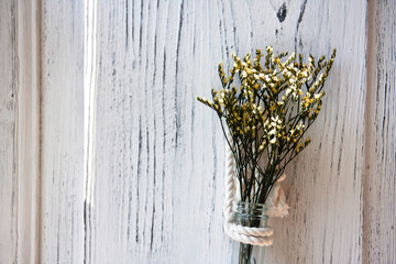 Yellow flowers in glass bottle hanging on a rope on white wooden background, interior decoration