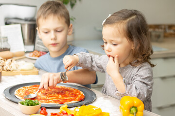 Obraz na płótnie Canvas Cute little girl 2-4 in gray dress and boy 7-10 in T-shirt cooking pizza together in kitchen. Brother and sister cooking