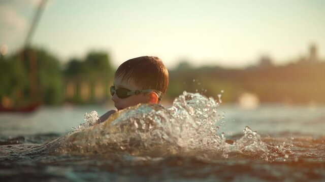 active young kid in water glasses swim in lake, river or ocean and play splash