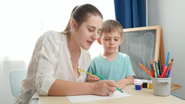 Smiing young mother drawing picture with her little son with pencils. Concept of parenting and education at home. Creativity and children art