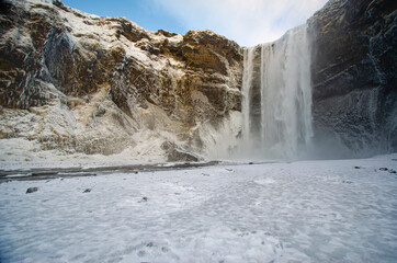 Waterfall Skógafoss on a winter day with snow-covered fields and people getting an up-close view of the waterfall.  