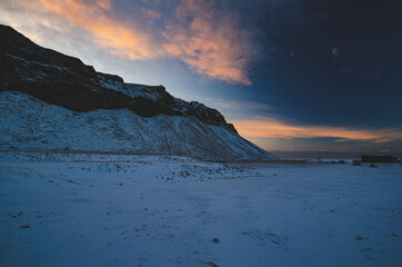 Sunrise behind a jagged snow-covered cliff in Iceland on a winter day. 