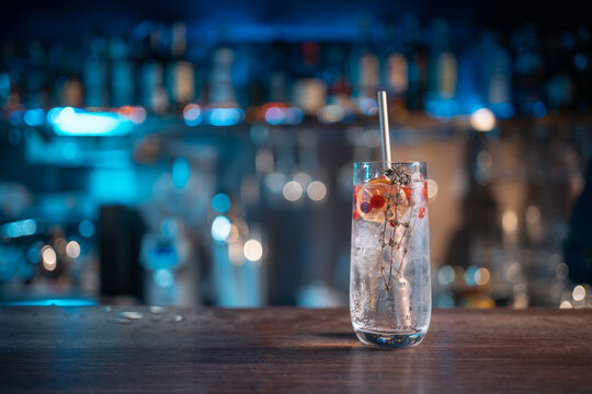 modern gin tonic cocktail with ice, straw and red berries on bar counter