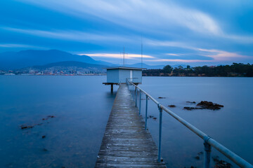 Boat shed and pier in the bayside suburb of Bellerive at twilight with the Hobart CBD and Mt Wellington in the background.