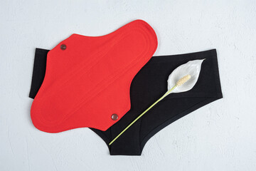 Eco reusable menstrual pad with white delicate flower and black underpants on grey background. Health care and zero-waste, no plastic concept. Top view Flat lay © IRINA