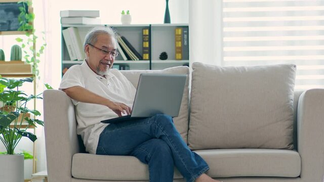 Happiness elderly asian man sitting on sofa and using computer laptop and smile at home,Senior lifestyle at home concept