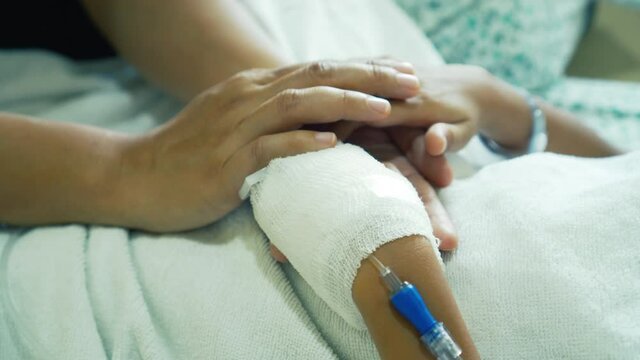 Young mother is holding hand bandaged of little daughter with comforting while they lying in the hospital bed sleeping. Recovering little girl. Hopeful emotional moment in ward. Focus on the hands.