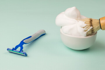 Disposable razor and shaving brush in a bowl of shaving foam.