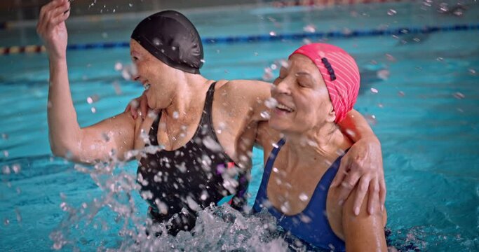 Senior women jumping splashing water having fun in indoor pool