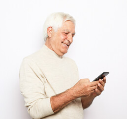 Tehnology and old people concept: Portrait of senior man who is messaging on smartphone over white background