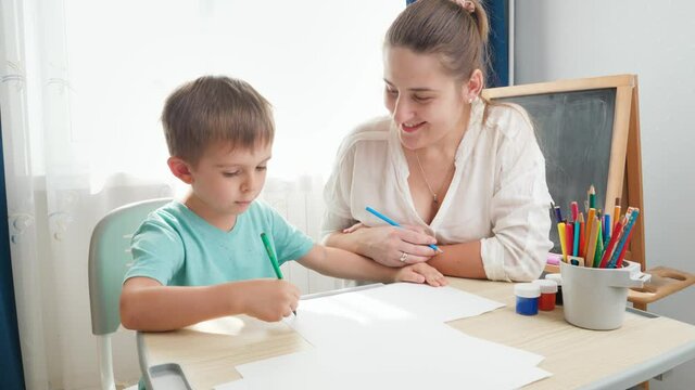 Young mother looking at her little son drawing or writing. Child learning drawing or writing at home during self isolation and lockdown