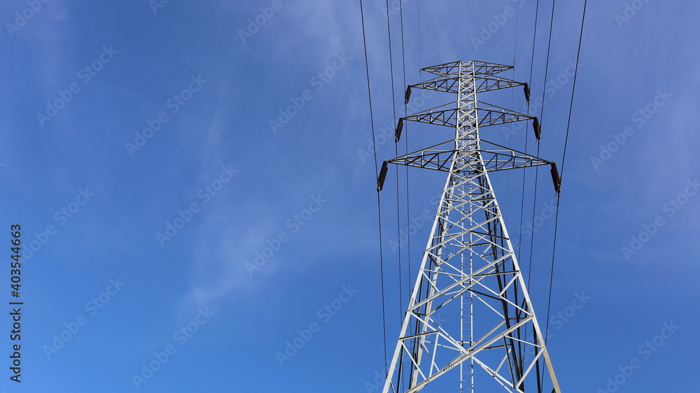 Wall mural High-voltage power lines. Steel structure of the three-level power transmission line tower with insulator in bottom view. On a blue background with a copy area. Selective focus