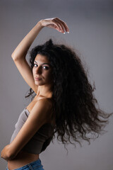 Beautiful brunette girl with long curly hair in the air, studio portrait on dark gray background