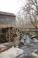 Mill house with a water wheel on a pond with a bridge and large rocks
