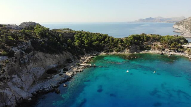 Scenic drone footage of crystal clear turquoise water of Anthony Quinn Bay in Rhodes in Greece. Motor boats parked in the bay, people snorkeling. Drony flying in the enclosed rocky bay.