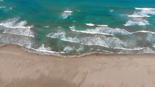 Scenic drone footage of Prasonisi peninsula in Rhodes in Greece surrounded by turquoise water. Aerial footage of a long sandy beach and waves breaking on the Aegean Sea.