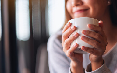 Closeup image of a beautiful young asian woman holding and drinking hot coffee in cafe