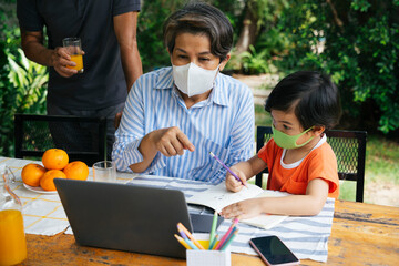 Grandmother and grandson wear mask learn how to drawn online with laptop.