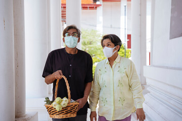 Asian senior elderly couple wear mask in a temple to make a merit.